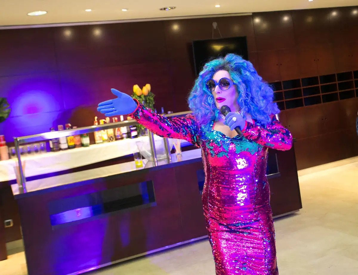 Drag queen con peluca azul y vestido de lentejuelas actuando en una cena baile